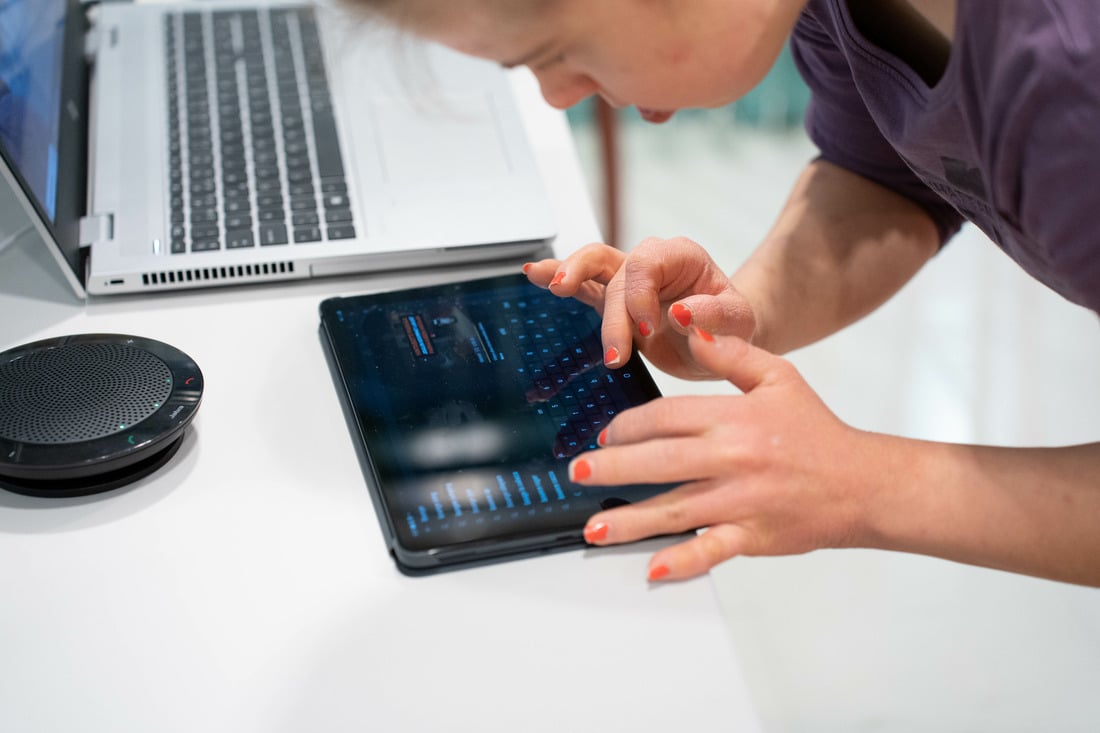 Henkilö kirjoittamassa tablet-tietokoneella. Tablet on pöydällä ja tabletin vieressä kaiutin ja kannettava tietokone.