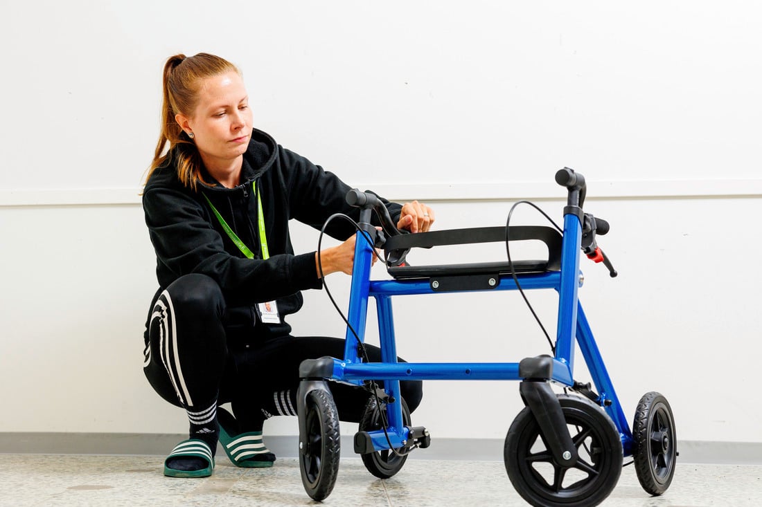 Nainen on kyykyssä ja säätää rollaattoria.