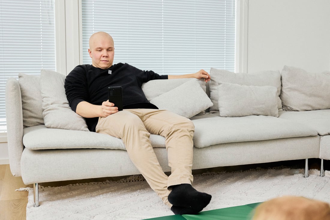 Mies istuu sohvalla matkapuhelin kädessä