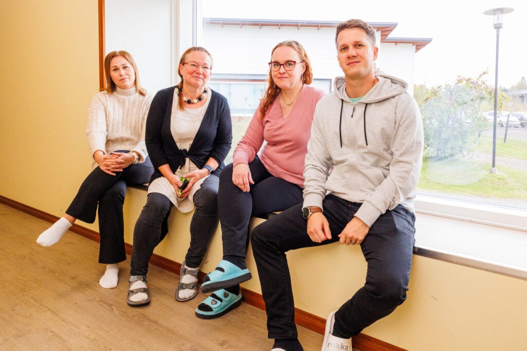 Neljä perhehoidon tuen tiimin ammattilaista istuu ikkunan edessä ja hymyilee kameralle.