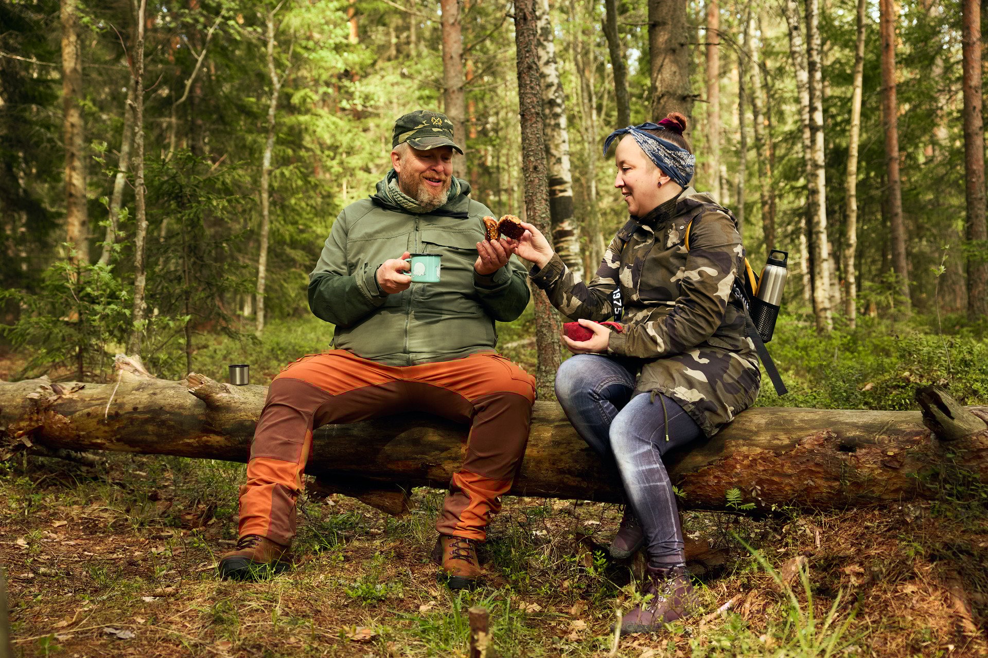 Kaksi ihmistä kahvittelee kaatuneella puun rungolla.