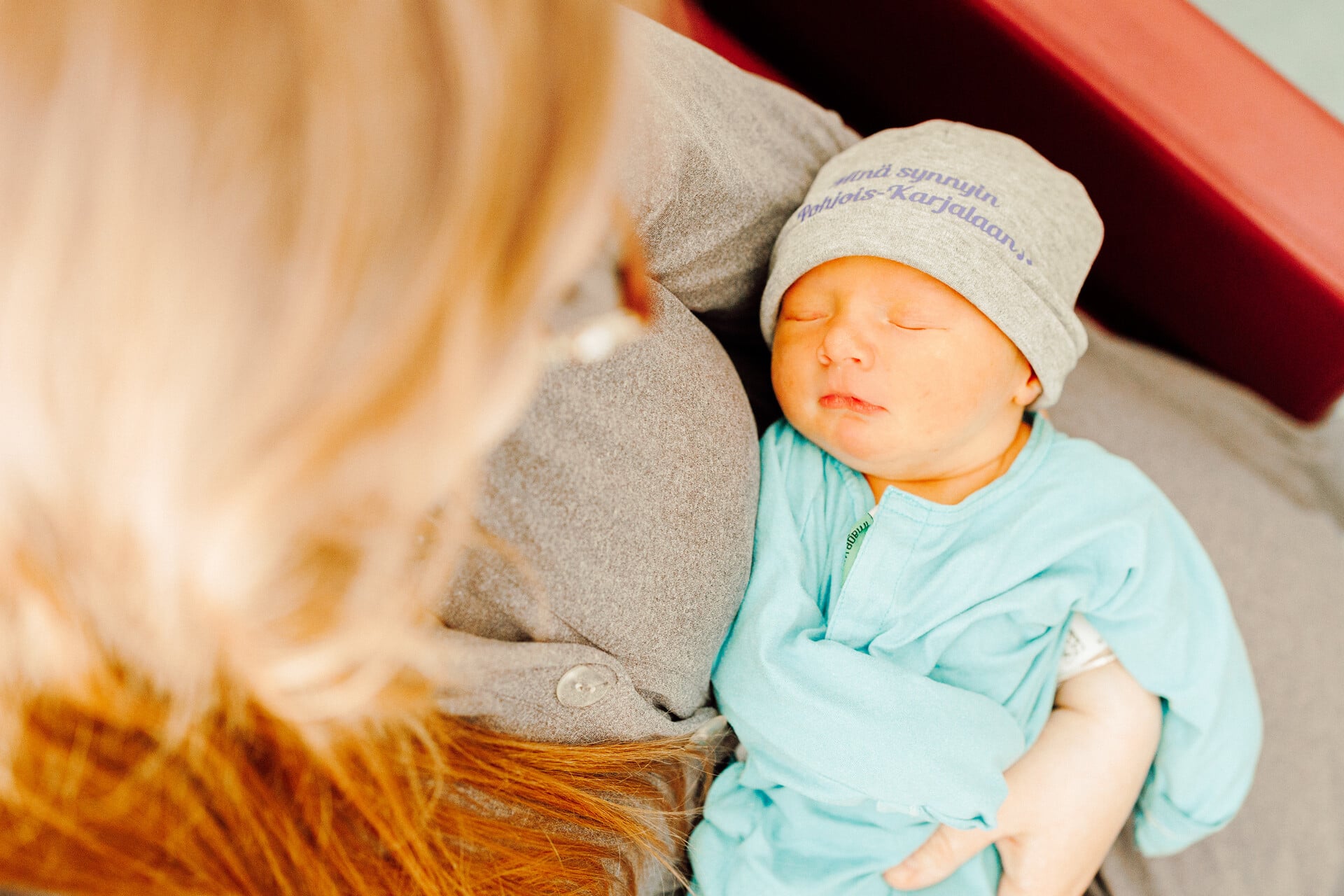 Sylissä vauva, jonka päässä on pipo tekstillä: Minä synnyin Pohjois-Karjalaan